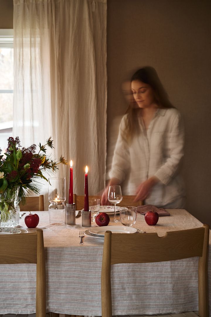 En kvinna dukar ett enkelt julbord med röda ljus, mönstrat julporslin och en enkel randig duk. 