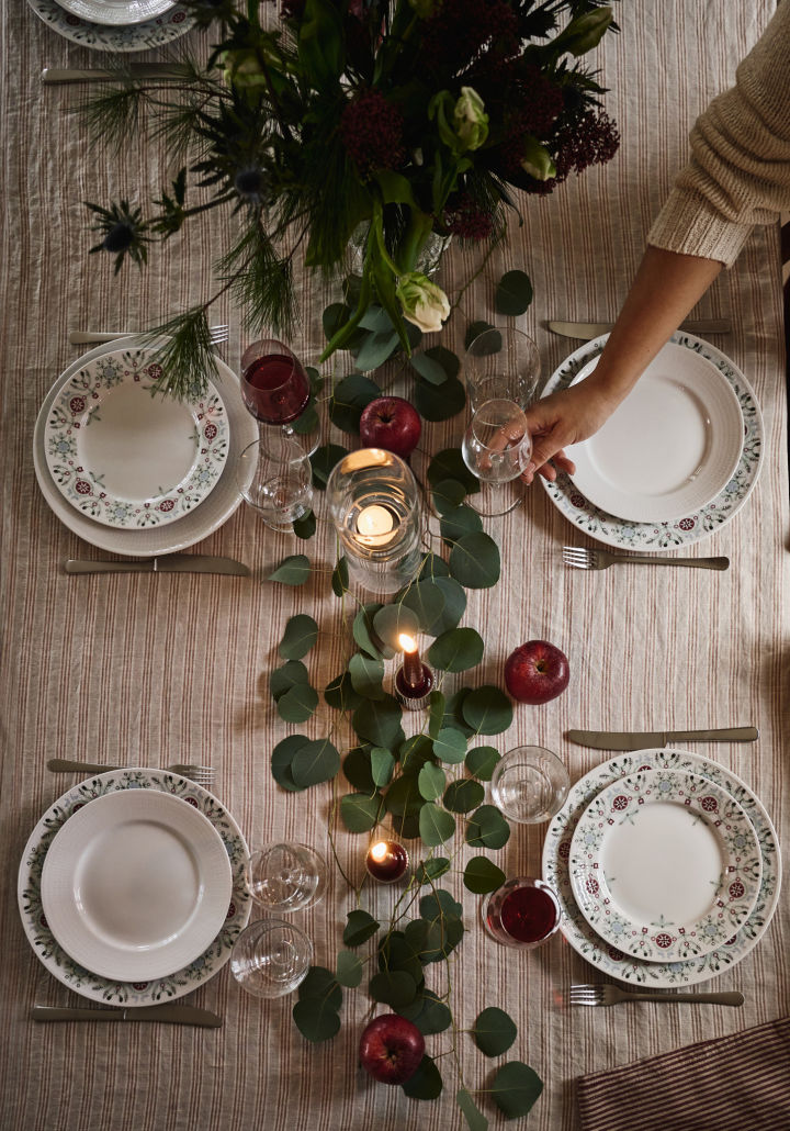 En enkel och elegant julbordsdukning fotograferad uppifrån med gröna blad och röda äpplen som dekoration.