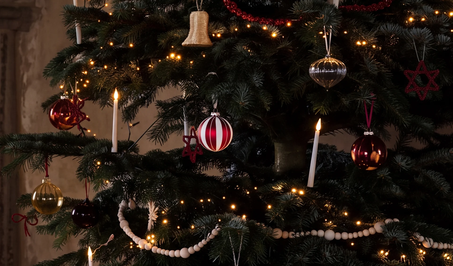 En dekorerad julgran med varma ljus, röda, silver och guld kulor, vita ljus och träpärlgirlander.