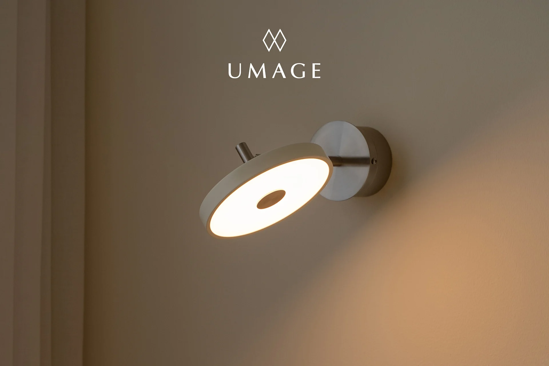 En modern cirkulär vägglampa med varmt ljus, monterad på en ljusbrun vägg. UMA-logotyp ovanför.
