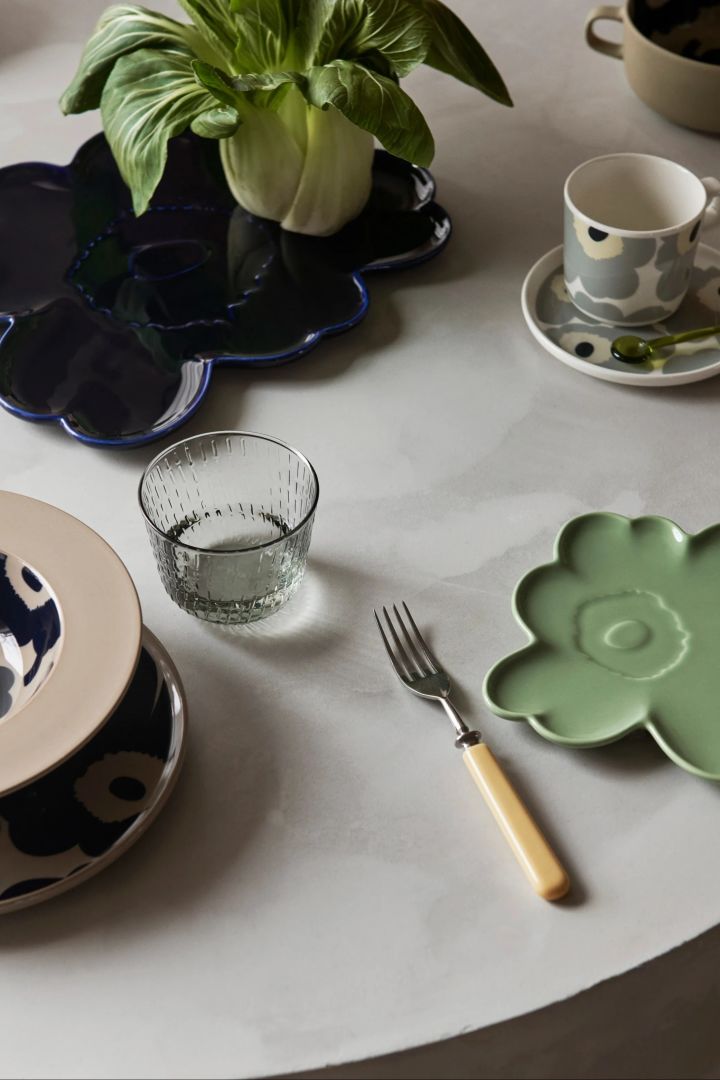 Dukning med Unikko-porslin från Marimekko, bland annat två blomsterformade fat i mintgrönt och mörkblått.