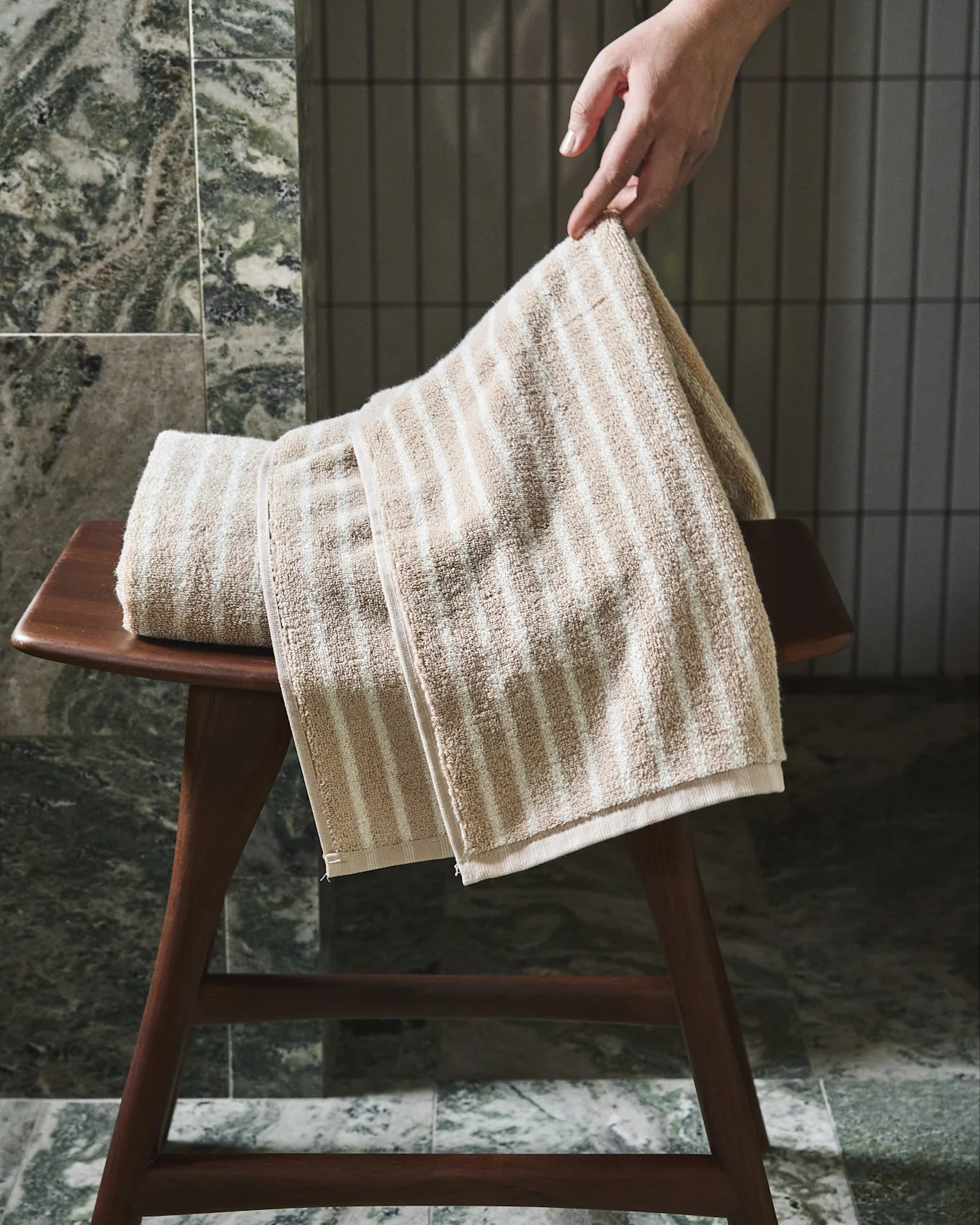 Hand som justerar en beige och vitrandig handduk på en träpall.