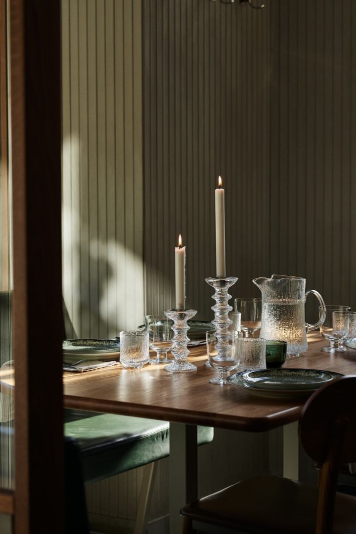 Här ser du en grön dukning i restaurangmiljö med grova ljusstakar i glas och matchande vattenkanna. 