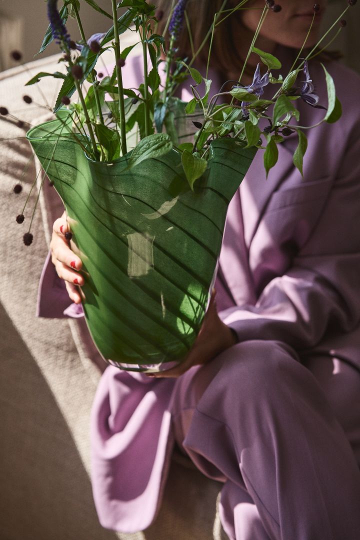 Person med lila kläder som håller den gröna glasvasen Tiggy från Byon, en vas med veckad, klockad form i ärtgrönt med ränder.