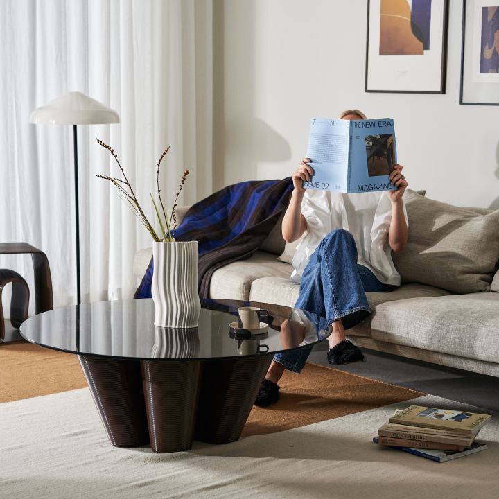 Inredningstips och de senaste inredningstrenderna att läsa om hos Nordic Nest. Här ett stilrent vardagsrum med brunt soffbord och kvinna som läser tidning.