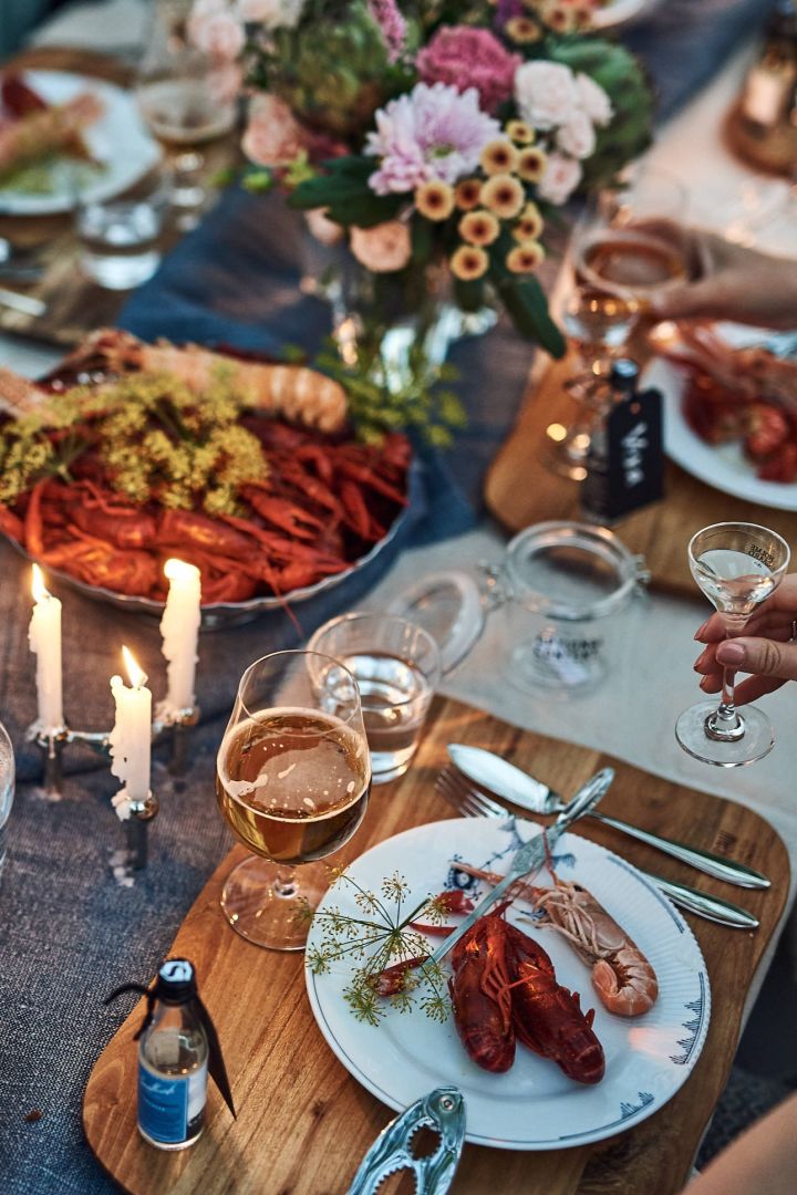 Kräftskiva med dukning i blåvitt med blåvitt porslin, detaljer i krom och kräftor i stor stål på ett väldukat bord.